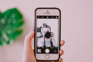 Hand holding phone with front screen picture of woman holding camera to face